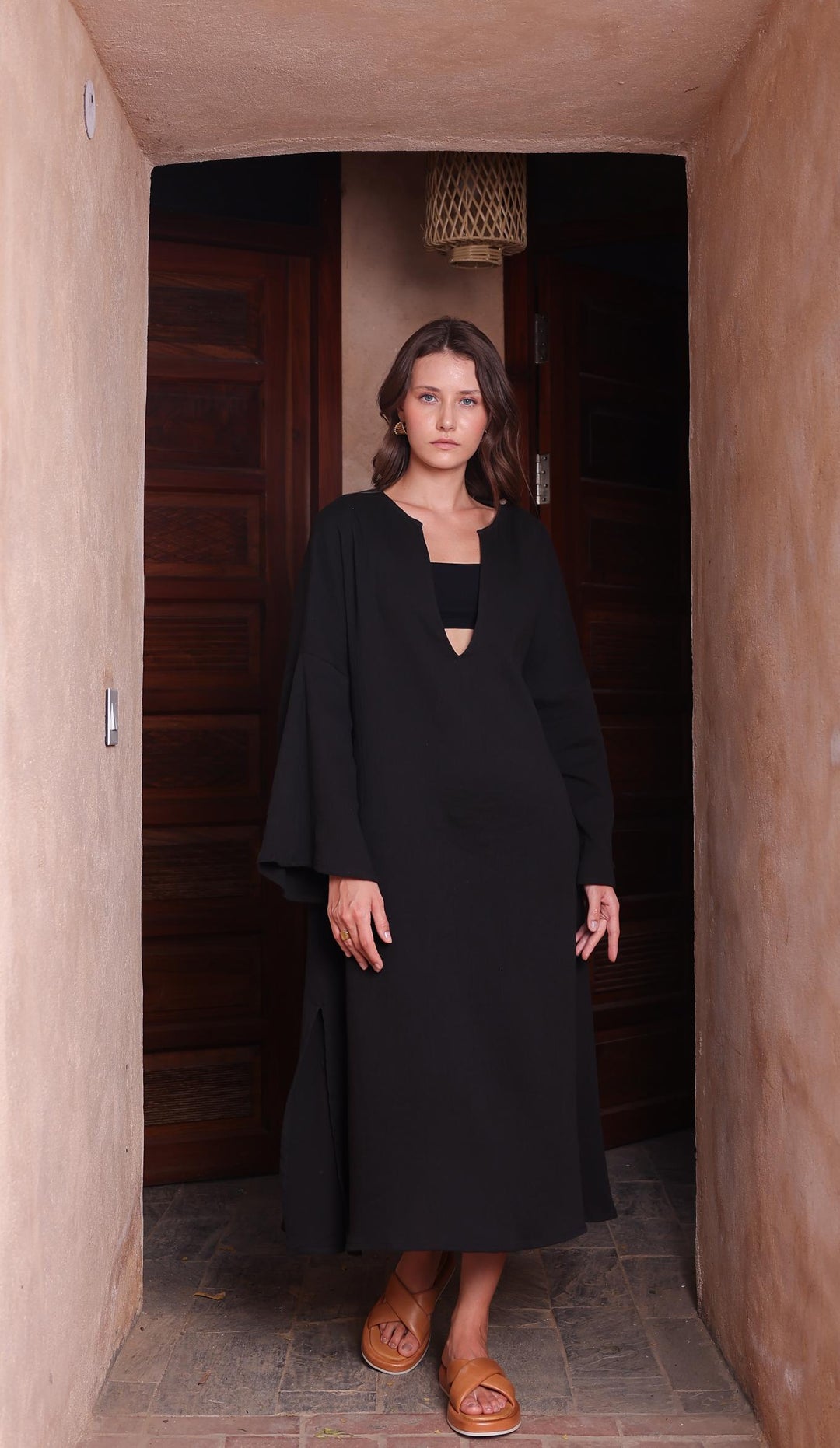 A woman in a flowing black Kiaan Kaftan from Thr3letter, featuring seersucker and organic cotton fabric.
