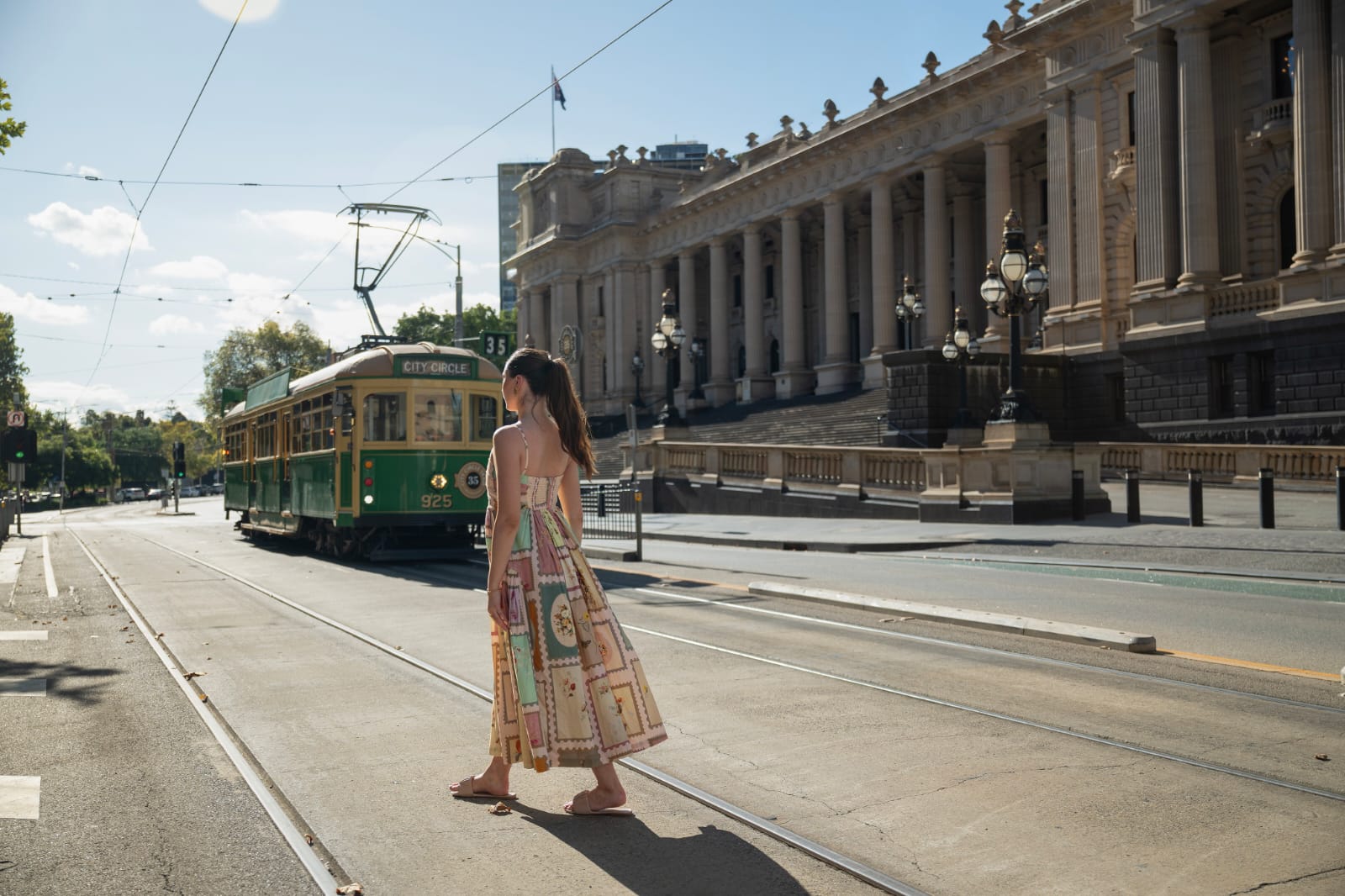 Woman wearing a butterfly print halter neck midi dress with a fitted bodice and pleated skirt, posing outdoors in natural light.