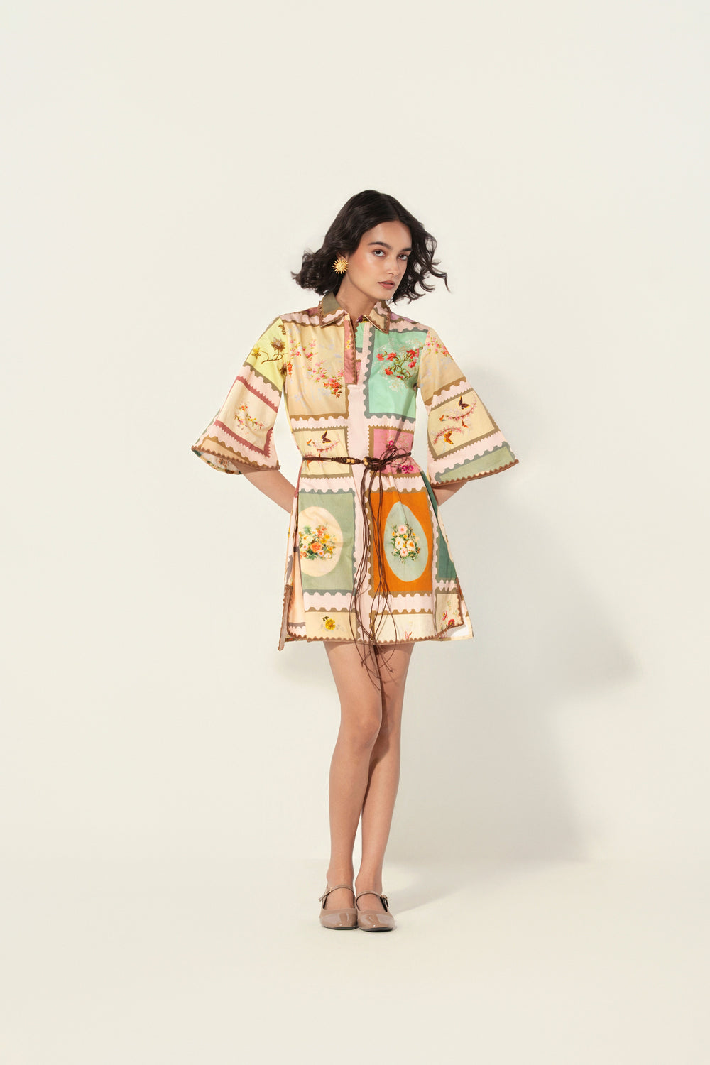 Woman wearing a pastel patchwork floral printed mini dress with a waist belt and with wide sleeves and a collared neckline from Thr3letter premium women's western wear collection.