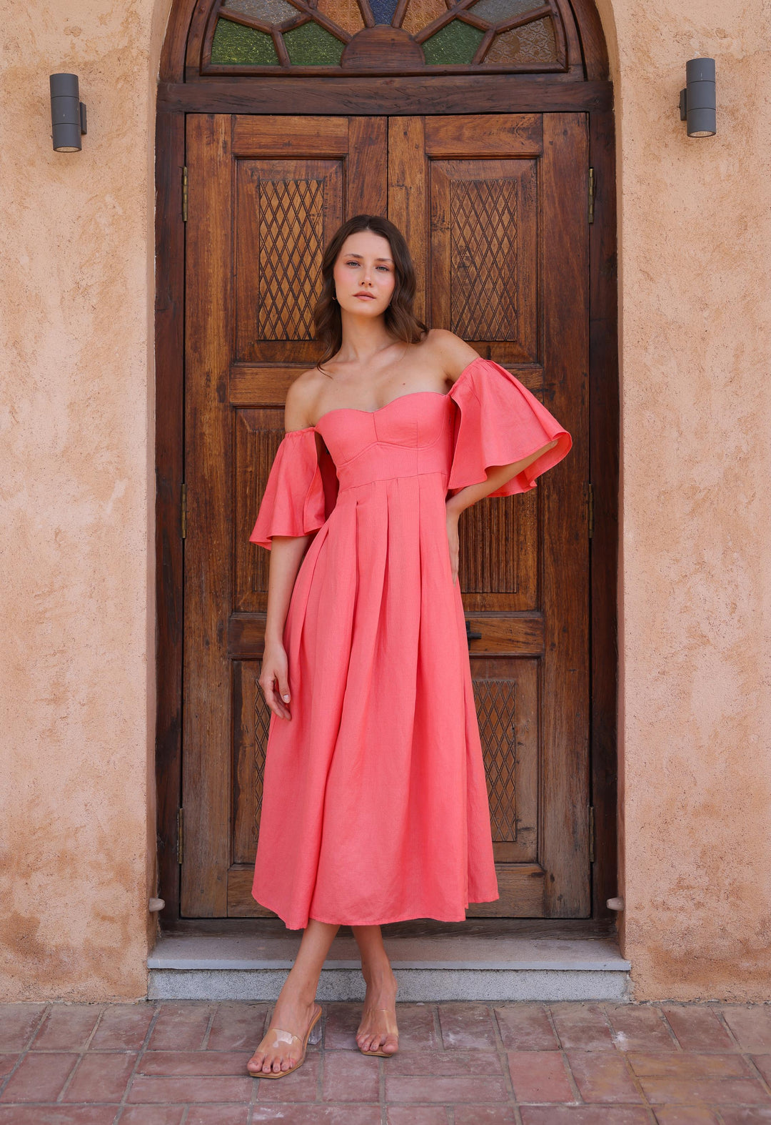 A young woman in a flowing Seraphina Dress by Thr3letter, standing in front of a wooden door with stained glass.